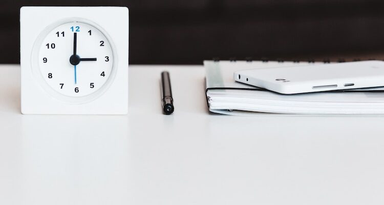 white desk clock near pen and book