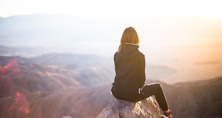 person sitting on top of gray rock overlooking mountain during daytime